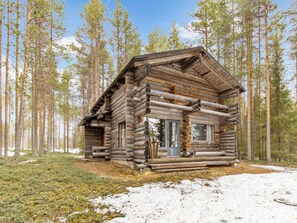A log cabin with a front porch, surrounded by a forest.