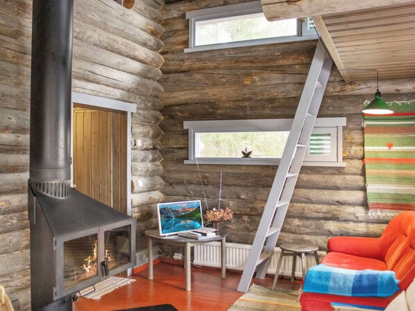 A log cabin interior with a fireplace, a painting, a ladder, and a colorful chair.