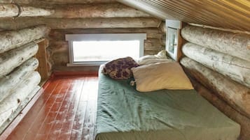Ein Blockhauszimmer mit einem Bett, einem Fenster und Holzboden.
