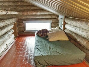 Une chambre dans un chalet en rondins, avec un lit, une fenêtre et un plancher en bois.