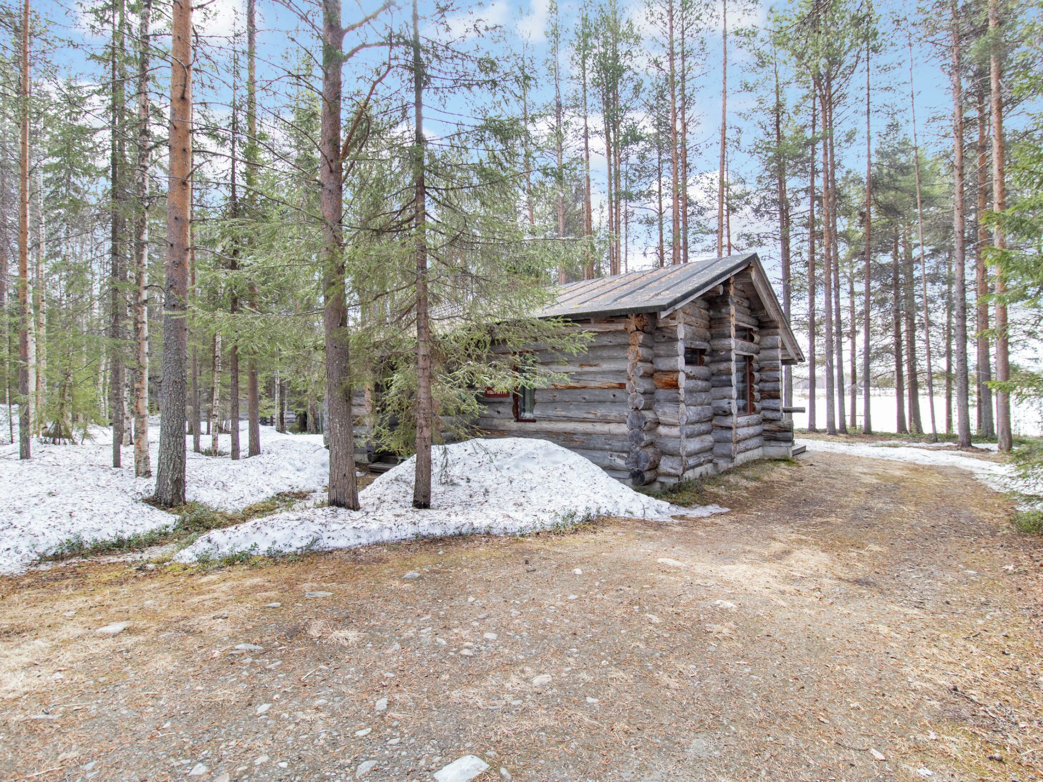 Eine Blockhütte im Wald, verbunden durch einen Feldweg.