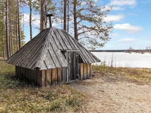A rustic wooden cabin with a sloped roof, situated in a forested area with a frozen lake in the background. - Kelopirtti by Interhome (Pelkosenniemi)