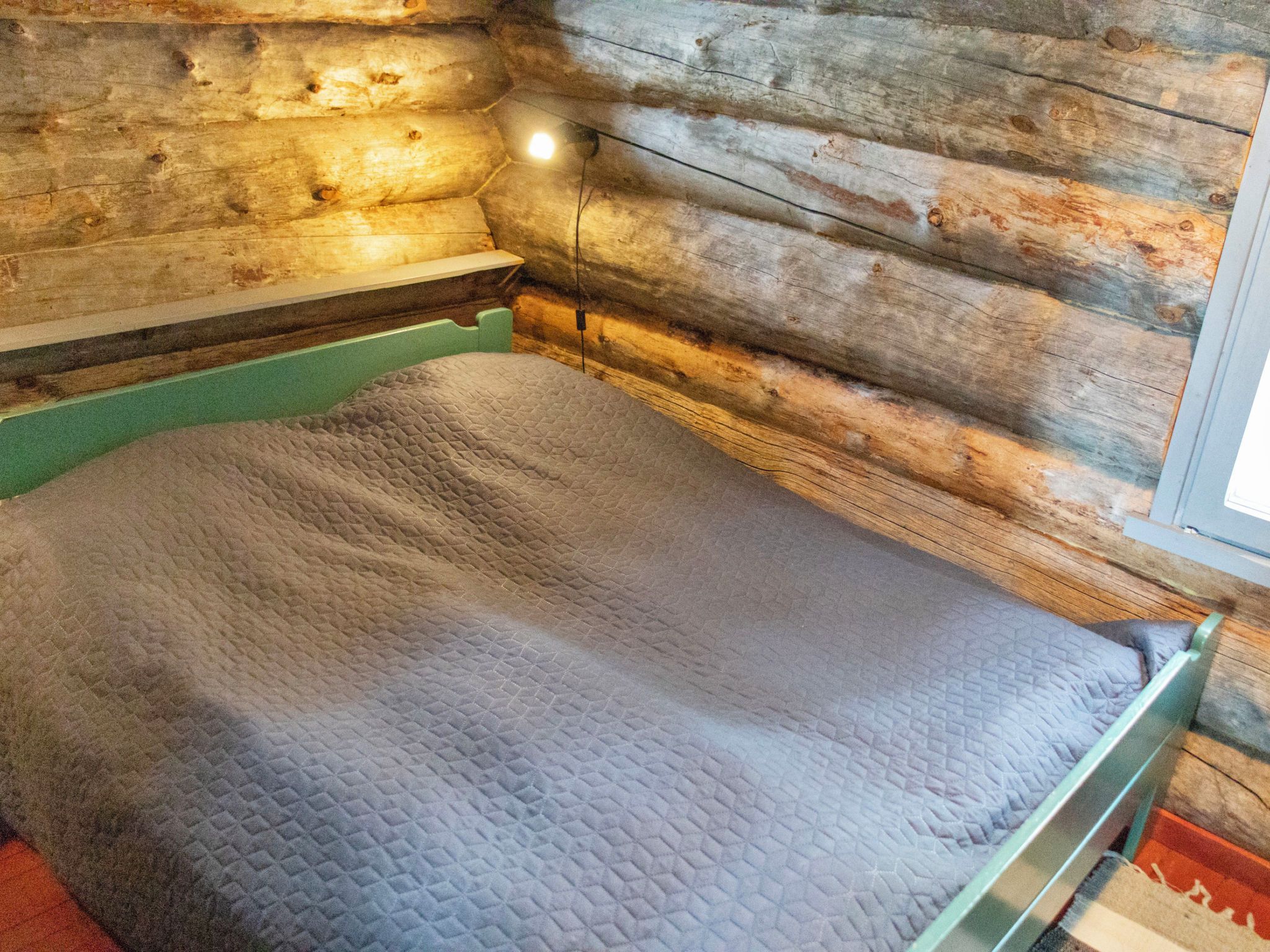 Cama em quarto de cabana de madeira, com moldura verde e colchão acolchoado.