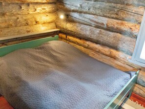 A bed in a log cabin room with a green frame and a quilted mattress.
