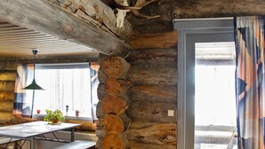A rustic interior with exposed wooden beams, a stone wall, a wooden table with benches, and a window with curtains.