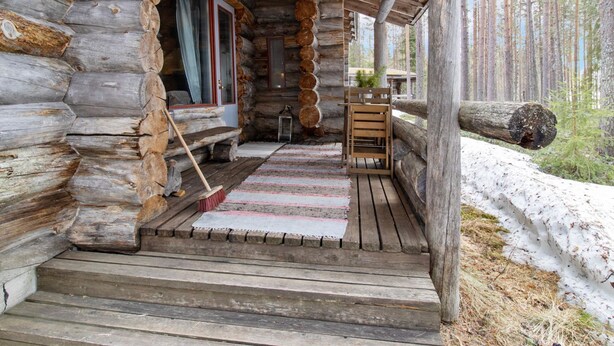 A log cabin with a wooden porch, a bench, and a small table.