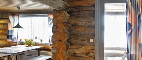Un intérieur rustique avec des poutres apparentes, un mur en pierre, un coin repas avec des bancs et une fenêtre agrémentée de rideaux.