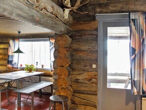 A rustic interior with exposed wooden beams, a stone wall, a dining area with benches, and a window with curtains.