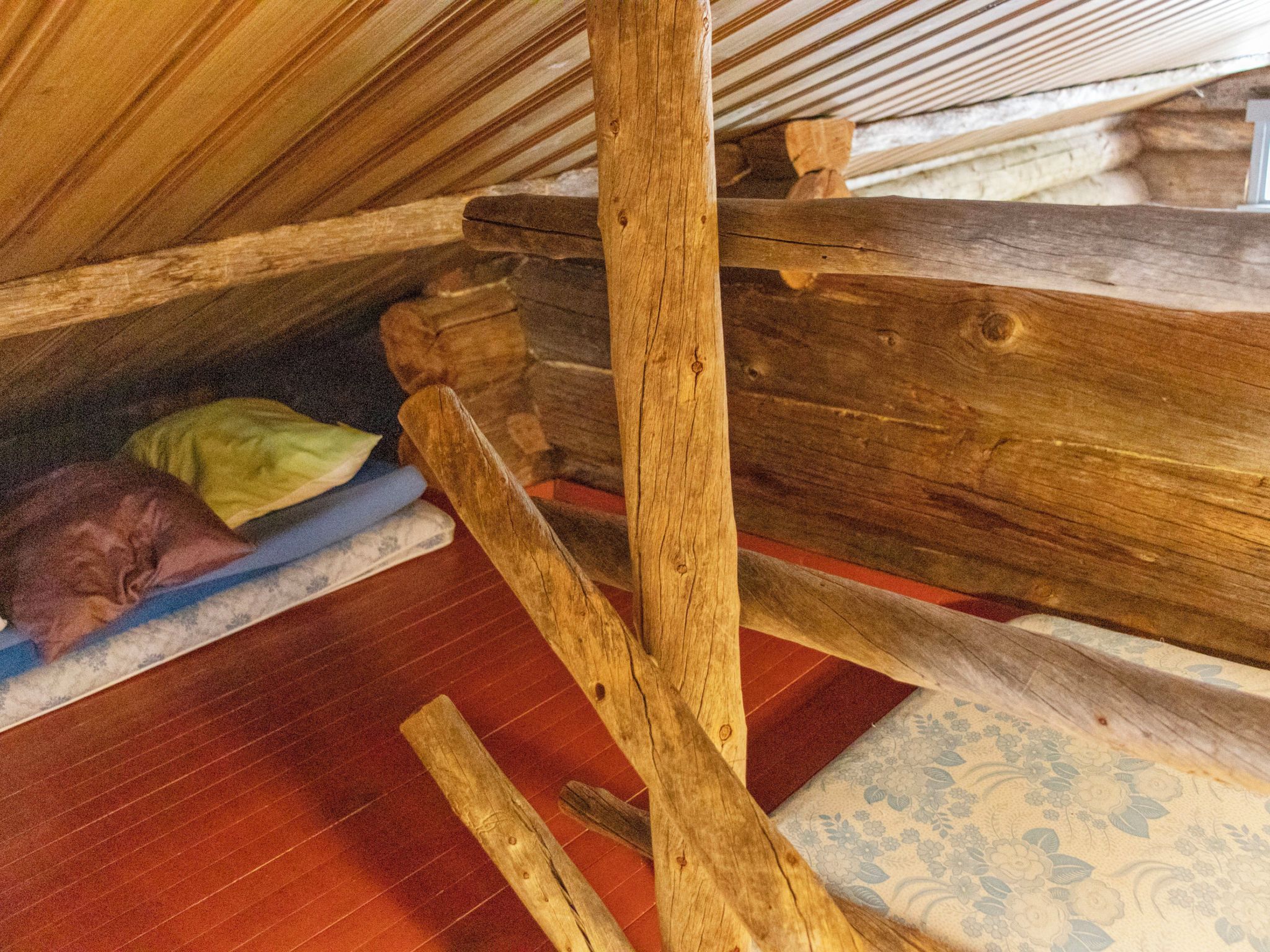 Une structure de plafond en bois avec un toit en pente, un matelas posé sur le sol et un tapis à motifs.