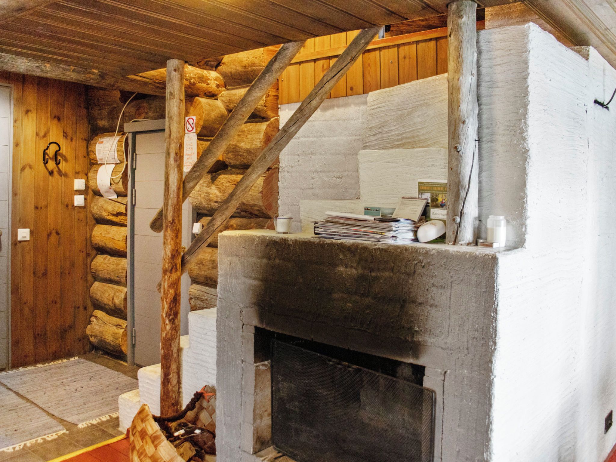 Interior rústico de una cabaña de troncos con chimenea, vigas de madera y un perchero junto a la puerta.