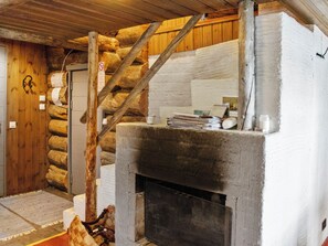 A rustic log cabin interior with a fireplace, wooden beams, and a door with a coat hanging on it.