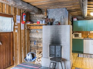 A rustic cabin interior with a stone fireplace, wooden walls, a small kitchen area, and a wooden door.