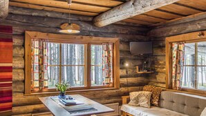 Ein gemütliches Blockhaus-Interieur mit einem Holztisch, einer Bank, einer Couch und großen Fenstern mit Vorhängen.