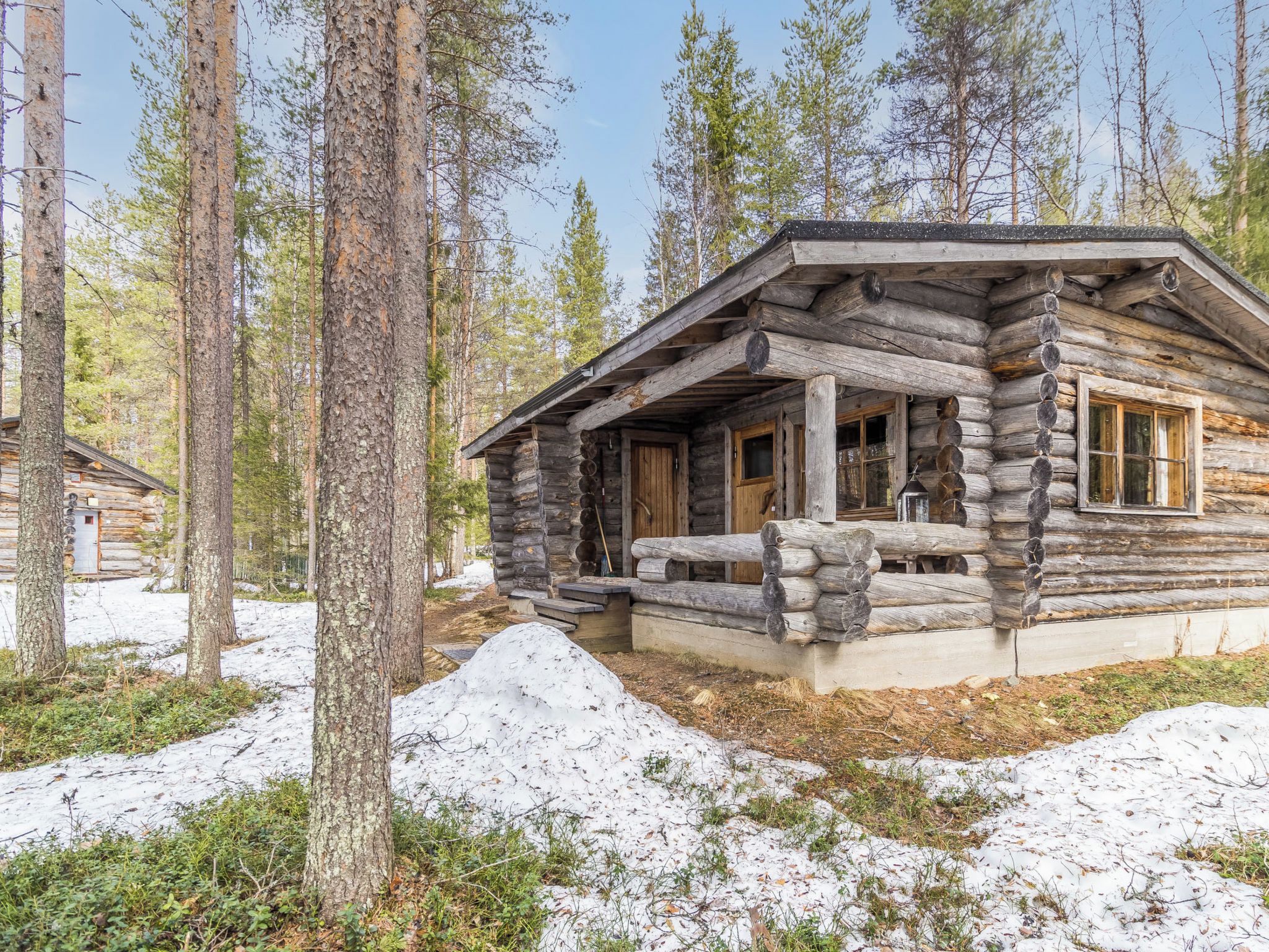 Une cabane en rondins avec un porche et une fenêtre, entourée d’arbres et de neige.