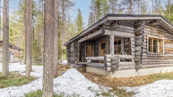 Una baita di legno con un portico e una finestra, circondata da alberi e neve.