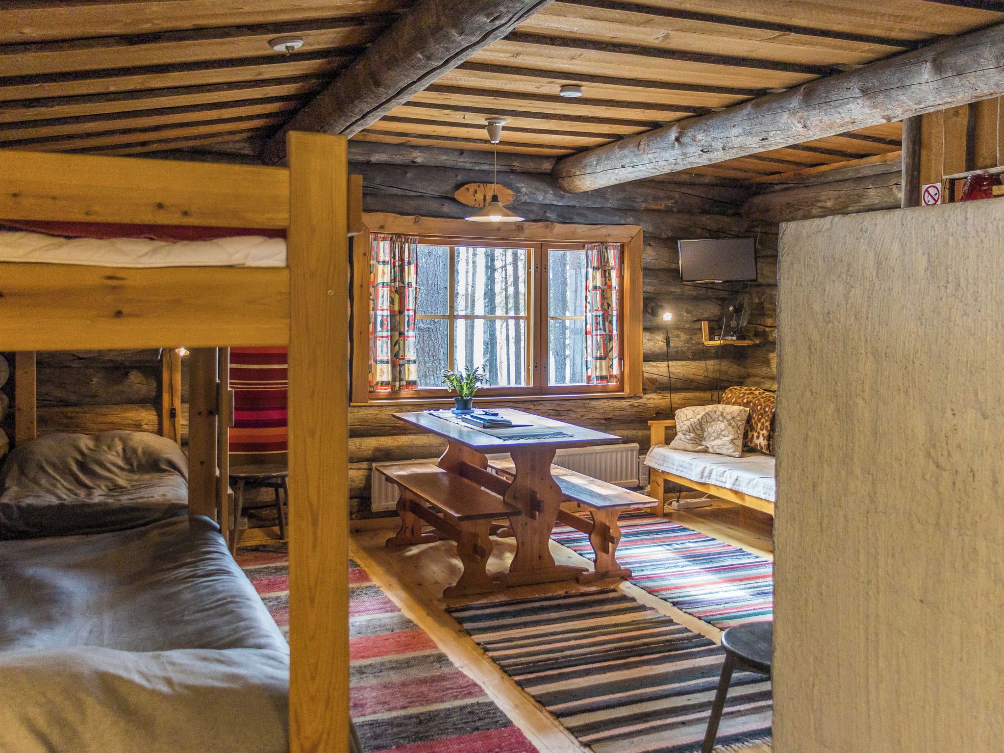 L’intérieur d’un chalet rustique, avec un plafond en bois, une table à manger, un canapé et une fenêtre avec des rideaux.