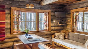 A cozy cabin interior with a wooden table, bench, sofa, and a television mounted on the wall.