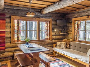 A cozy cabin interior with a wooden table, bench, sofa, and a television mounted on the wall.