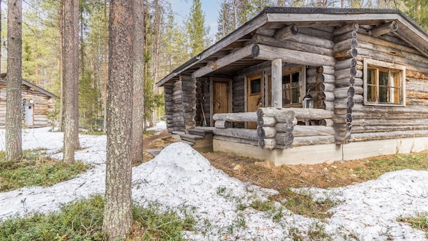 Eine Blockhütte mit Veranda, umgeben von hohen Bäumen und Schnee.
