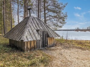 Une cabane en bois rustique, dotée d’un toit en pente, entourée d’une forêt et d’un lac gelé.