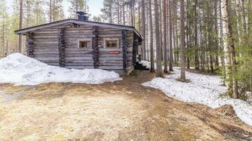 Una cabaña de troncos con chimenea, ventana y puerta, rodeada por un bosque y nieve.