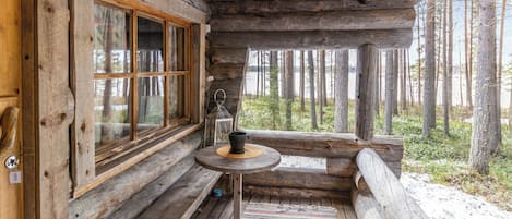 A rustic cabin interior with a wooden bench, a small table with a cup, and a window overlooking a forest.