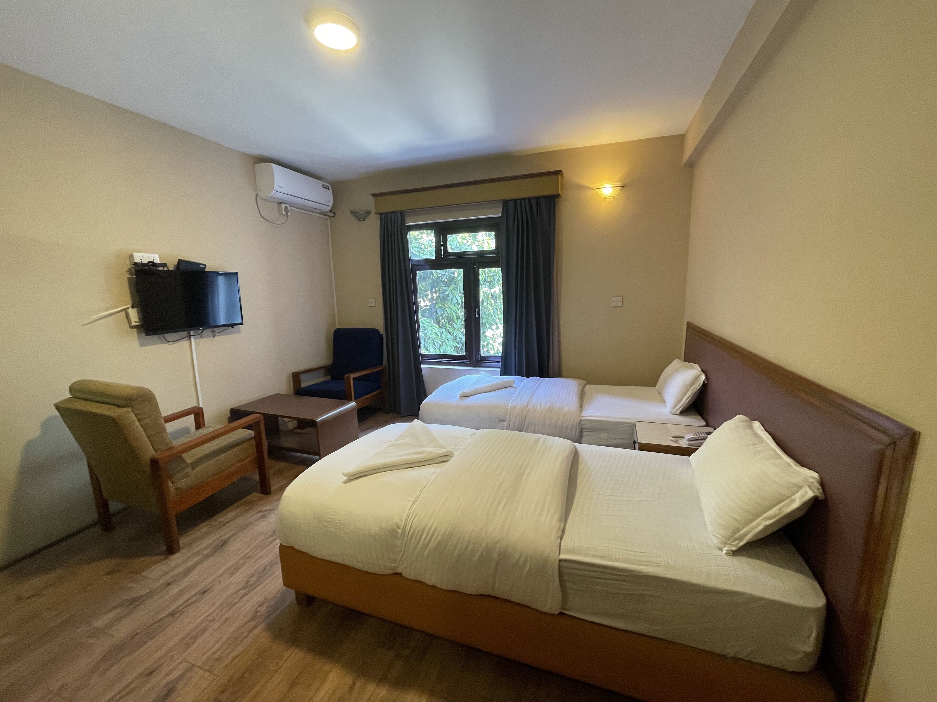 A hotel room with two beds, a desk, a chair, a TV, and a window with curtains.