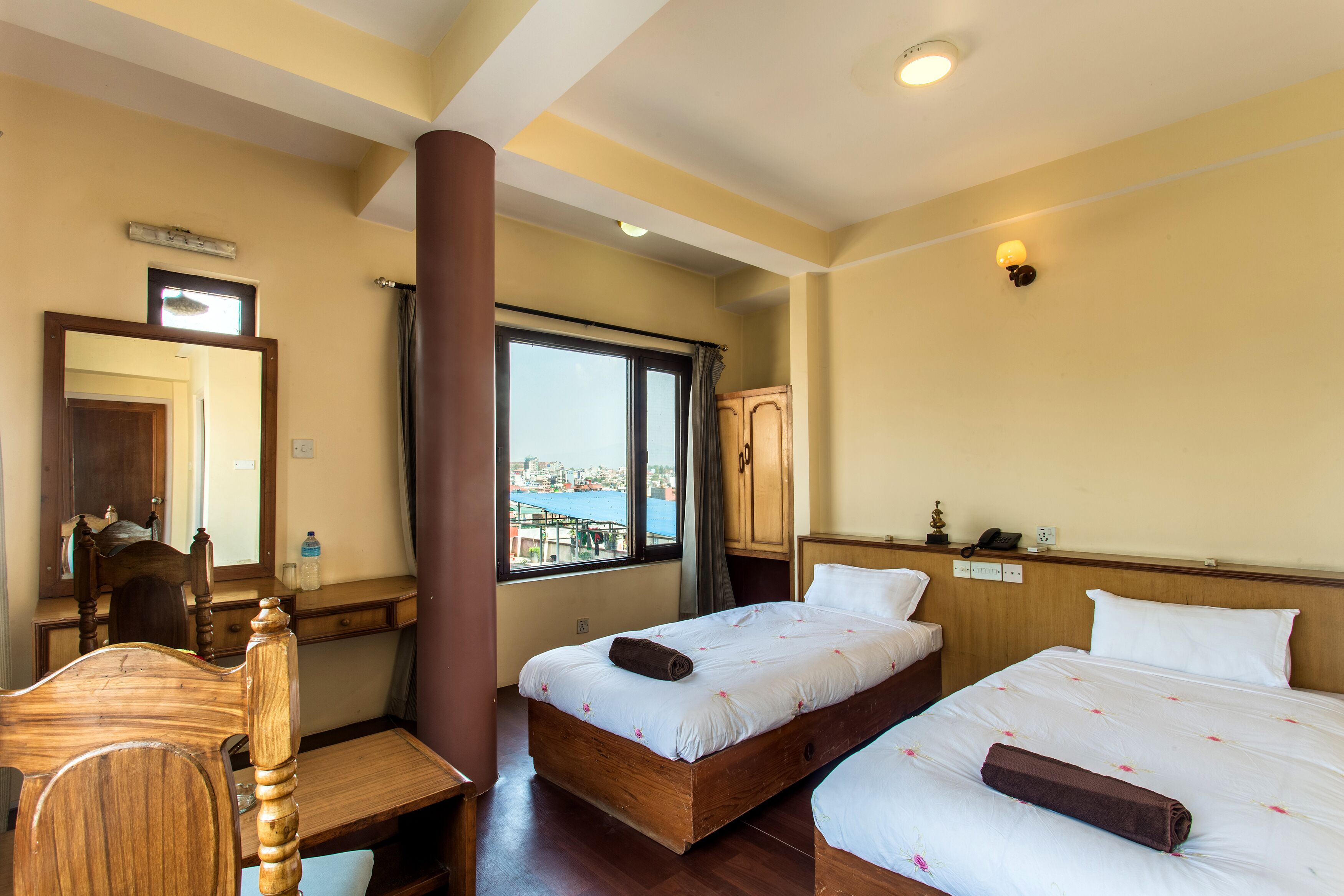 Habitación de hotel con cama y escritorio de madera, un espejo y ventana con vista a un cuerpo de agua.
