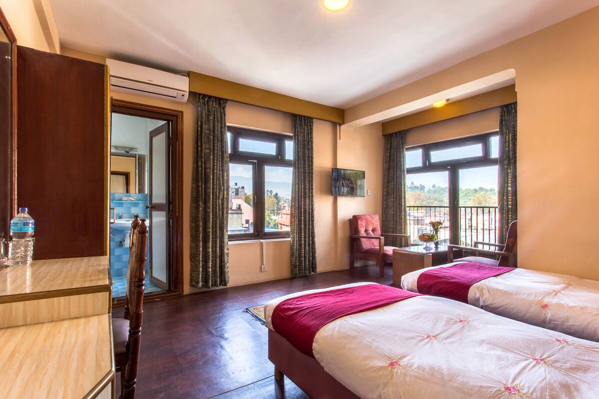 Habitación de hotel con dos camas, un escritorio, una silla, televisión y balcón con vistas.