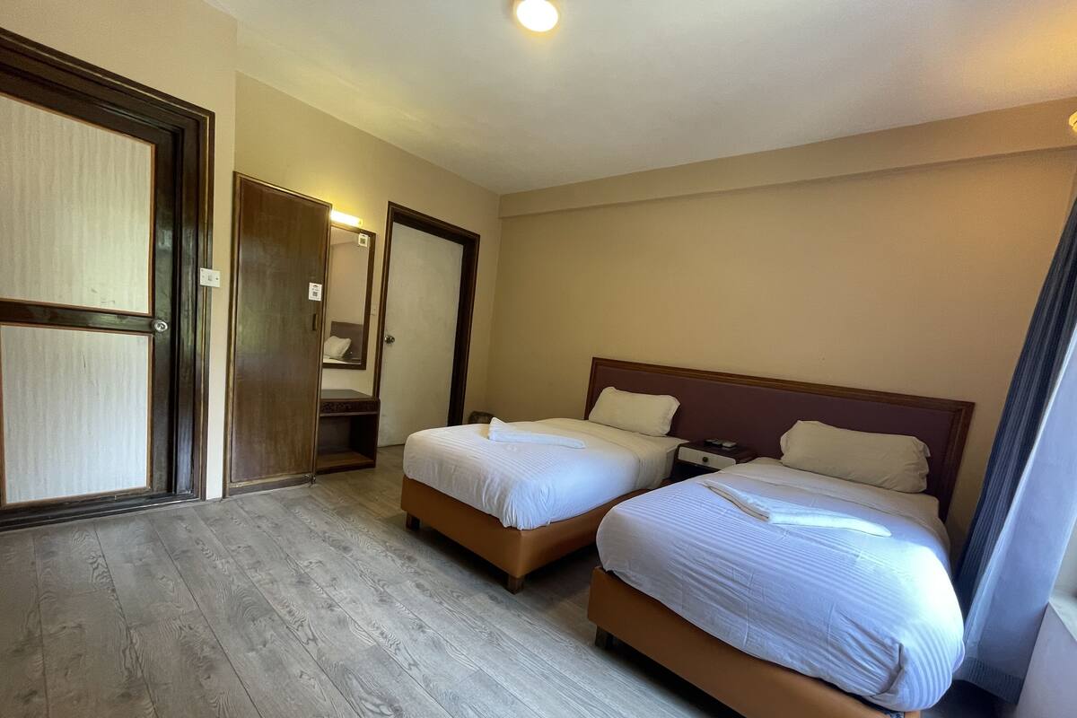 Habitación de hotel con dos camas, suelo de madera, un espejo grande y una puerta corrediza.