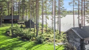 A cabin with a grassy yard, a small shed, and a body of water in the background.