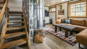 A rustic interior with a wooden staircase, a large metal water heater, a sofa, and a fireplace.