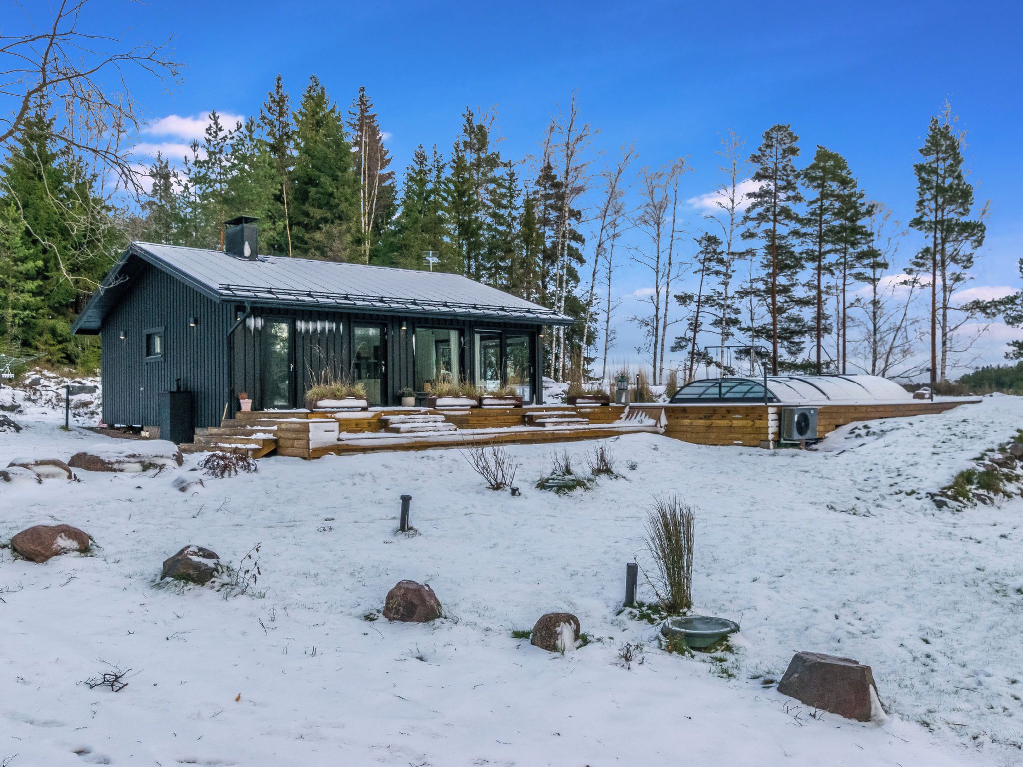 A cabin with a large deck and a covered outdoor area, surrounded by snow and trees.