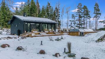 A cabin with a large deck and a covered outdoor area, surrounded by snow and trees.