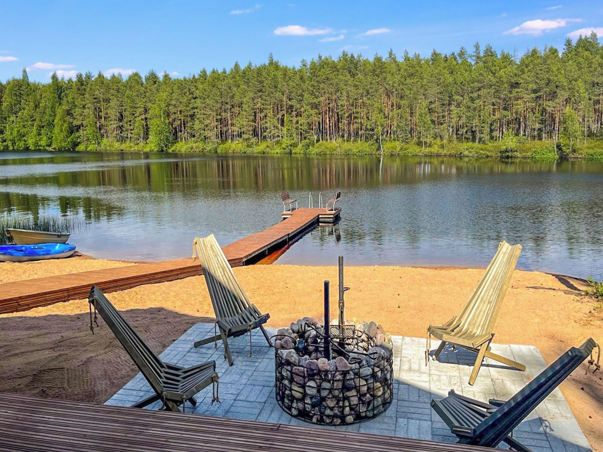 A lakeside deck with lounge chairs, a fire pit, and a dock extending into the water.