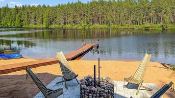 A lakeside deck with lounge chairs, a fire pit, and a dock extending into the water.