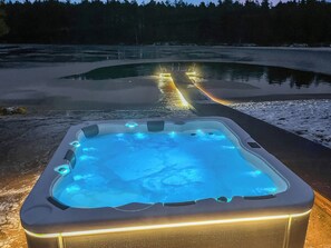 Un bain à remous avec une terrasse en bois qui s’étend sur une étendue d’eau, le tout entouré d’un paysage enneigé.