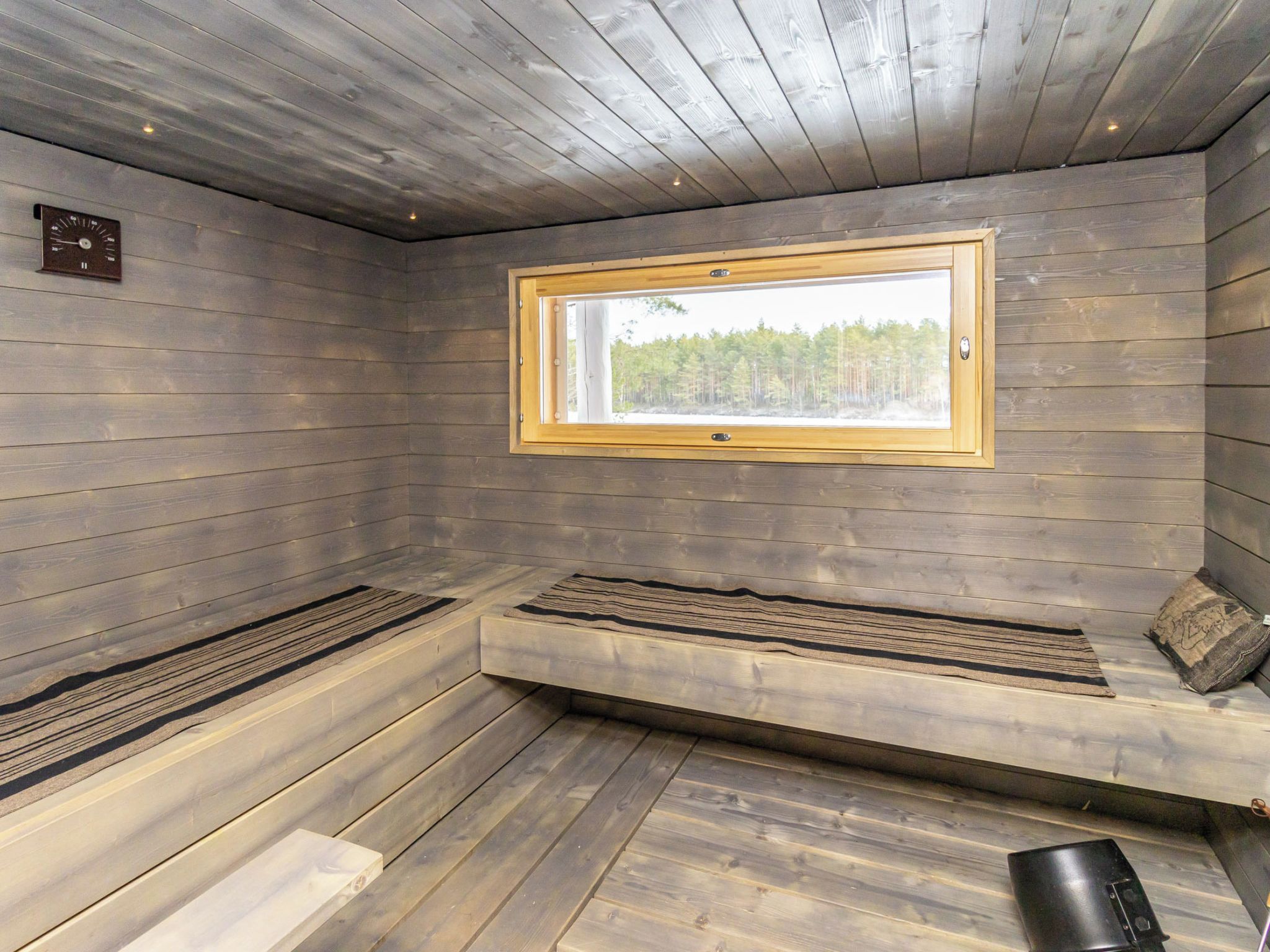 A sauna room with wooden walls, a bench, a window, and a clock.