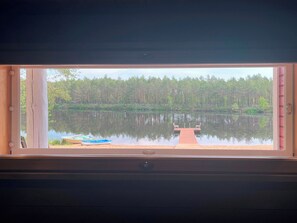 Ein Fenster mit Blick auf einen ruhigen See, eine Anlegestelle und einen Wald.