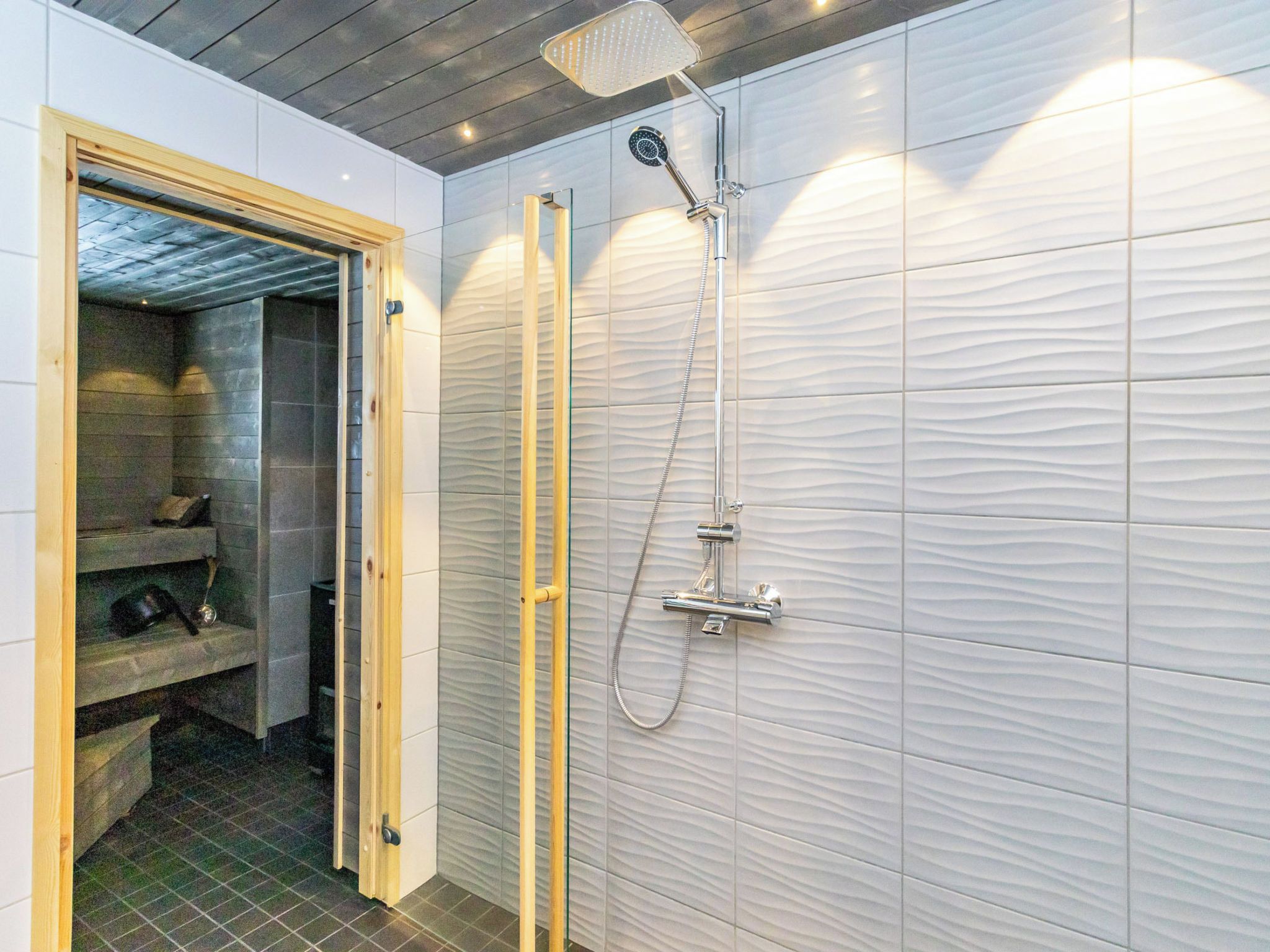 Ein modernes Badezimmer mit Dusche, einer Holztür und einer gefliesten Wand.