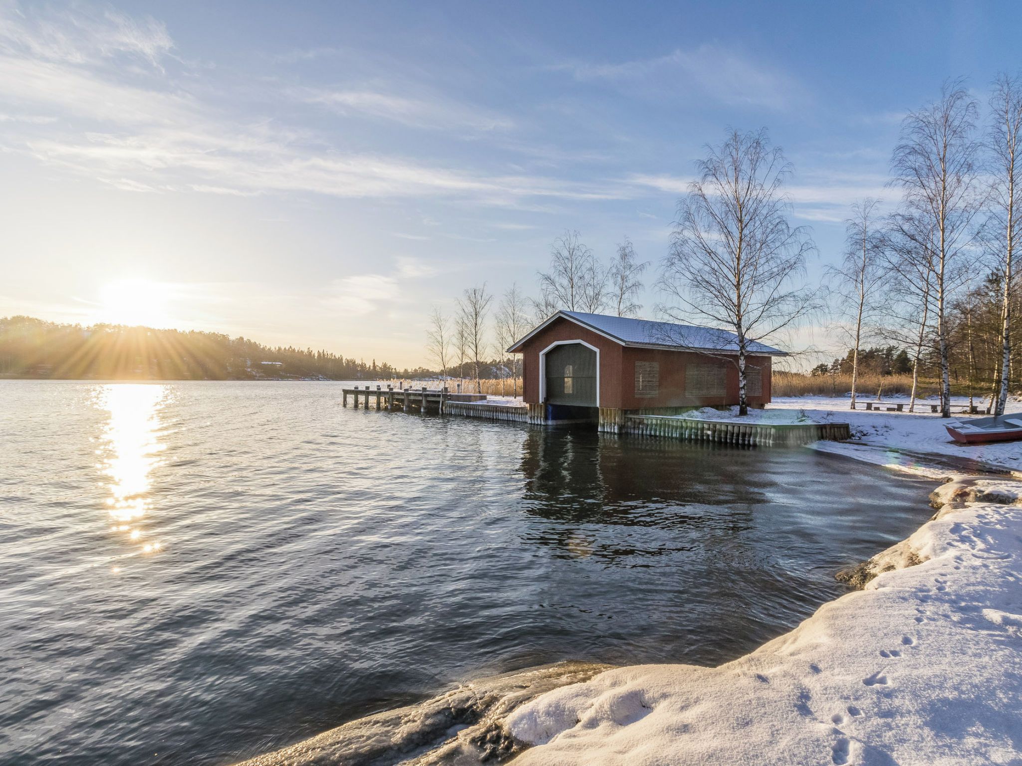 A wooden boathouse by a frozen lake with a dock extending into the water.