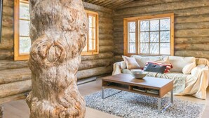 A log cabin interior with a large tree trunk in the foreground, a sofa, a coffee table, and two windows. - Kaasavuoren ranta by Interhome (Naantali)