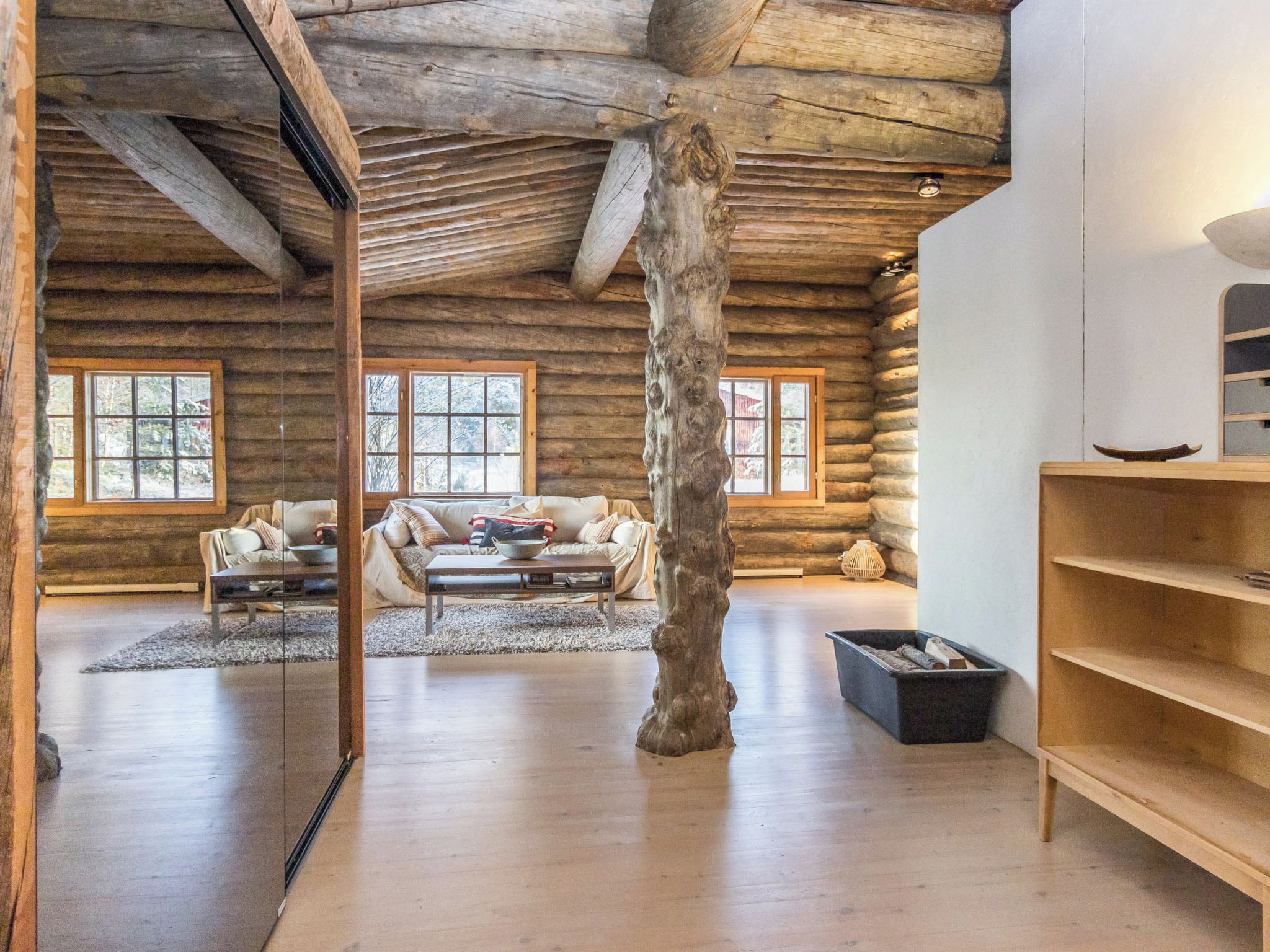 A log cabin interior with a sofa set, a coffee table, and a large wooden tree trunk centerpiece.
