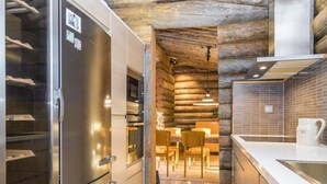 A modern kitchen with stainless steel appliances, a wooden log wall, and a dining area with wooden chairs. - Kaasavuoren ranta by Interhome (Naantali)