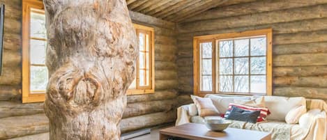 A log cabin interior with a large tree trunk, a sofa, and a coffee table.