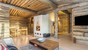 L’intérieur d’une cabane en rondins comprend un coin repas, une cheminée et un téléviseur.
