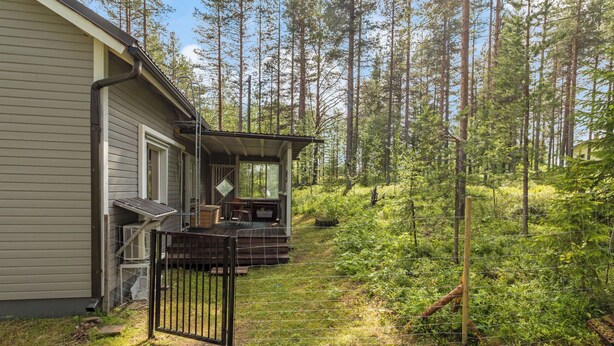A house with a covered porch, a fenced yard, and a forested area.
