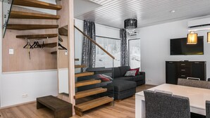 A modern interior with a staircase, a sofa, a dining table, and a TV.