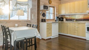 A cozy kitchen with wooden cabinets, a dining table with chairs, and a clock on the wall. - Puljunharju by Interhome (Sodankylä)