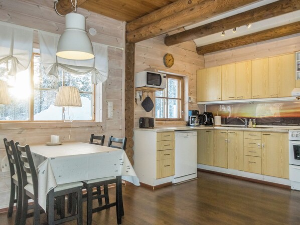 Une cuisine chaleureuse avec des meubles en bois, une table à manger entourée de chaises et une fenêtre donnant sur des arbres couverts de neige.